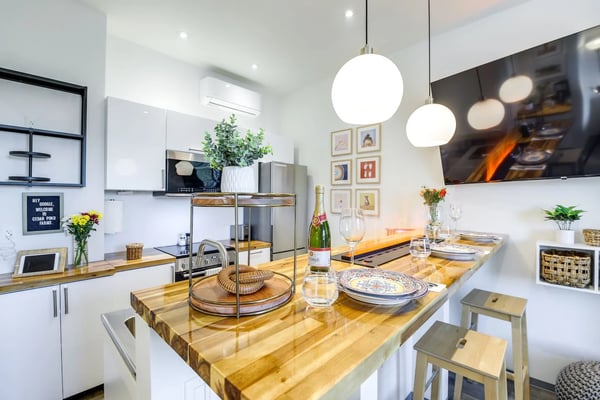 Modern kitchen and dining area with white cabinetry, wood countertops, pendant lights, and place settings on the island counter